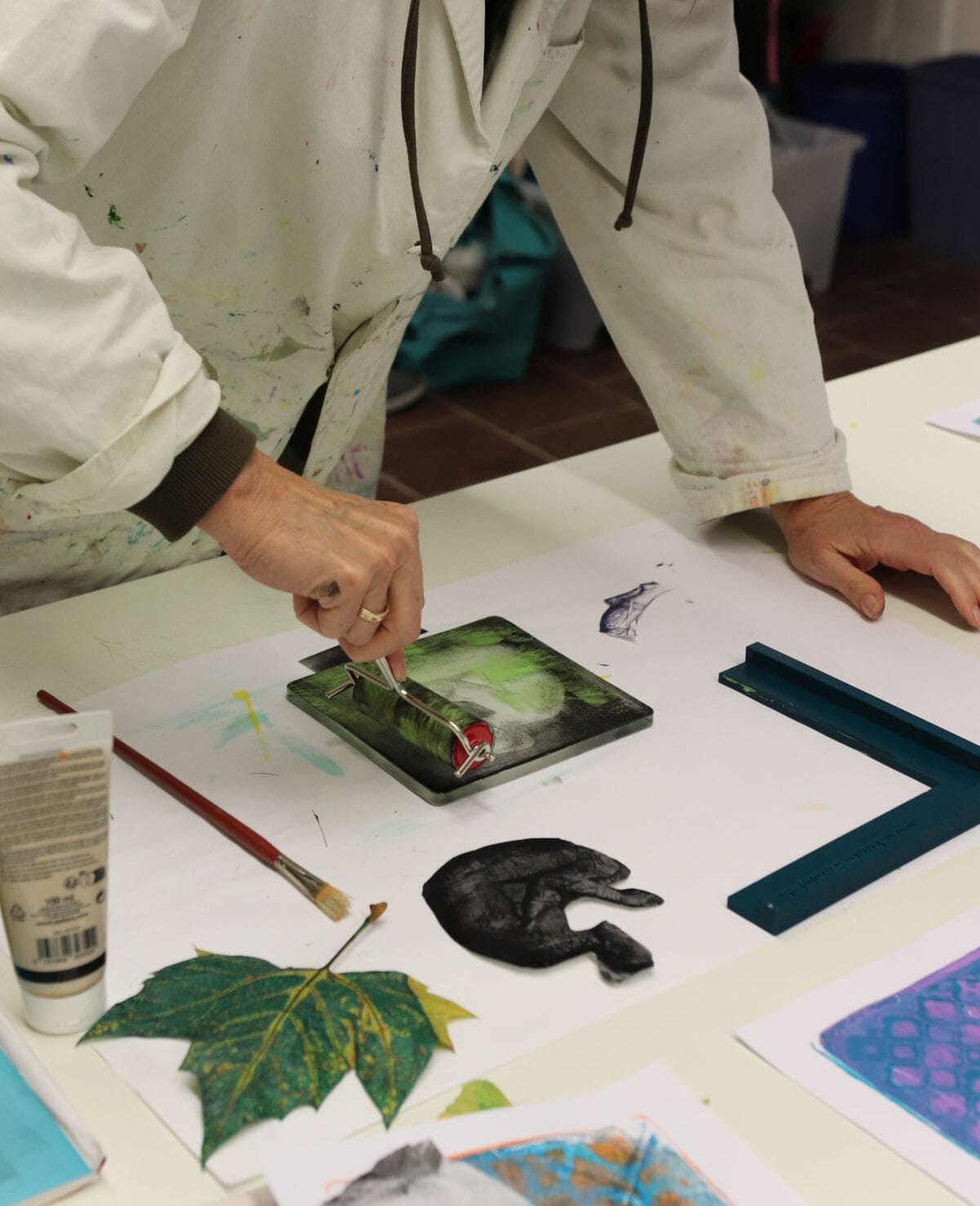 Teilnehmerin rollt Acrylfarbe mit einer Farbwalze auf eine Druckplatte im Kreativworkshop